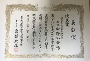 松伏町立第二中学校教諭・中野和幸が、平成23年度教育実践報告会において優良賞を受賞し、教育公務員弘済会埼玉支部より助成金とともに表彰された表彰状。埼玉県公立中学校美術科教員時代の教育実績を示す資料。