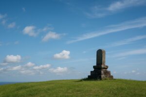 開けた丘と空のワンカット（人物は小さめ）／碑は斜めから一瞬