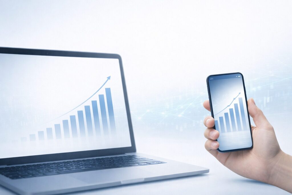 ノートPCとスマートフォンに表示された金融チャートで、SageMasterの仕組みやAIによる補助的な資産形成を表したイメージ