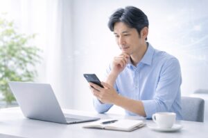白と淡いブルーの背景、40代〜50代の日本人男性が静かにスマートフォンやノートPCを見ながら落ち着いて考えている構図、忙しい日常の中でも未来のために判断しているイメージ、背景にごく薄く金融やAIを感じる要素、感情ではなく冷静に向き合う人を表現、清潔感、知的、信頼感、シンプル、上品、余白多め、文字なし、広告っぽくない、怪しくない Japanese man in his 40s to 50s calmly looking at smartphone or laptop, thoughtful but not anxious, concept of a busy person making calm decisions for the future, subtle finance or AI feeling in background, white and soft blue background, clean, elegant, intelligent, trustworthy, minimal, lots of white space, no text, realistic, blog header image, easy to compress, no excessive details, no complex textures, 16:9 horizontal